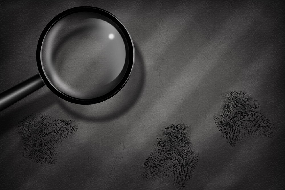 Criminology: A magnifying glass positioned over—or very close to—a tabletop that features three distinct fingerprint impressions.