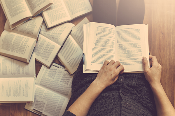 Woman reading with books along the floor beside her.
