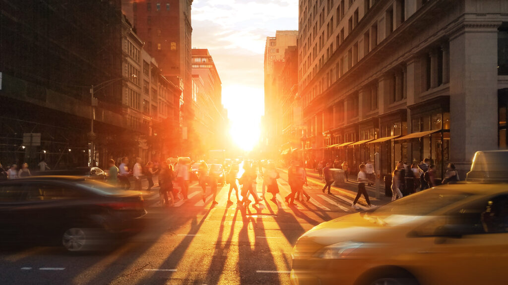 Crowds of people and cars in the busy intersection on 23rd Street and 5th Avenue in New York City with sunset shining in the background