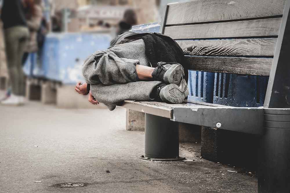Social Inequality: Poor homeless man or refugee sleeping on the wooden bench on the urban street in the city.