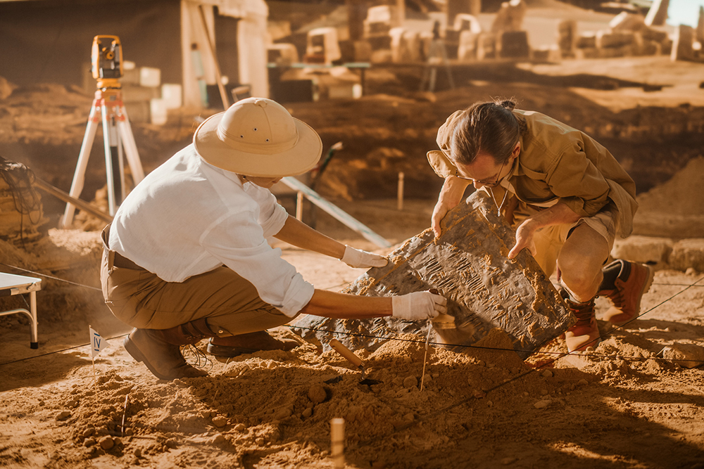 Archaeological Digging Site: Two Archeologists Work on Excavation Site, Carefully Cleaning, Lifting Newly Discovered Ancient Civilization Cultural Artifact, Historic Clay Tablet, Fossil Remains